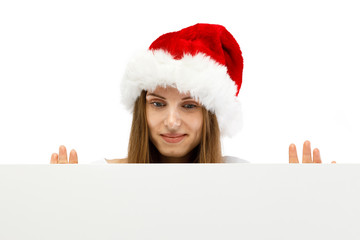 Beautiful woman in Santa Claus clothes peeking behind blank board on white background