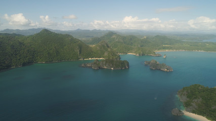 Aerial view of Groups islands with sand beach and turquoise water in blue lagoon among coral reefs, Caramoan Islands, Philippines. Mountains covered with tropical forest.