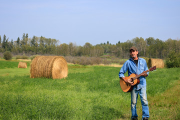 Naklejka na ściany i meble Handsome man playing a and acoustic guitar in the field