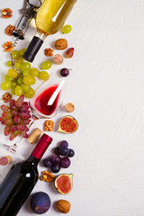 Glass and bottle of wine with fruits and nuts on white background. Wine still life with copy space. top view, vertical