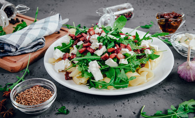 Dish with Arugula on a white plate. Green, fresh arugula on a plate, with white cheese and pasta on a stone countertop. The concept of preparing a fresh and healthy salad. Caring for health.