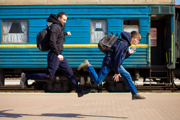 Obraz premium Two man with big bags run at railway station. Travel by train