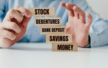 Risk of investing, dangerous financial instruments. Put wooden blocks with the words SAVINGS, DEBENTURES, STOCK. Investing is associated with a waste of money, a catastrophe.