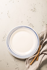 Empty white plate, napkin and cutlery on grey stone background