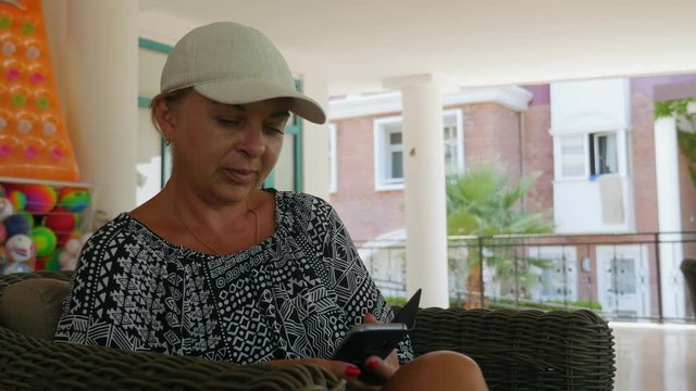 Blond woman in a white cap is surfing the net on her smartphone in a patio   