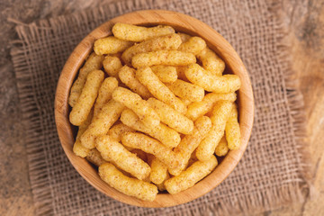 Crispy corn sticks in wooden bowl on burlap napkin