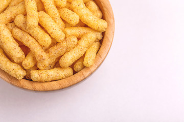 Crispy corn sticks in wooden bowl on light background