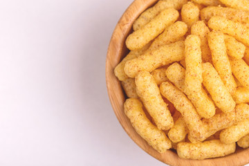 Crispy corn sticks in wooden bowl on light background