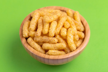 Crunchy corn sticks in wooden bowl on bright colored background