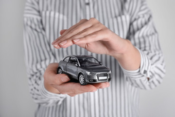 Insurance agent covering toy car on grey background, closeup