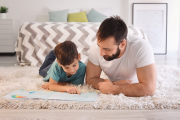 Fototapeta premium Cute little boy and his father reading book at home