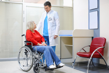 Male doctor taking care of mature woman in wheelchair indoors
