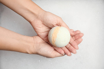 Woman holding bath bomb over foam, top view