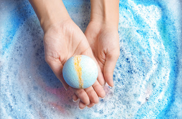 Woman holding color bath bomb over foam, top view