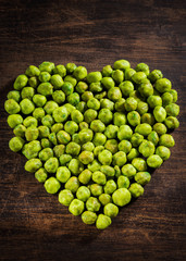 Homemade Dry Spice Wasabi Peas as an Appetizer in heart shape on wood background.