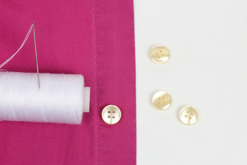 Coil with white threads and a needle and sewn pearl buttons on the shirt