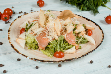 Fresh salad caesar salmon closeup on brown plate on white textured table with cherry tomatoes and chilli and pepper spices and green at background