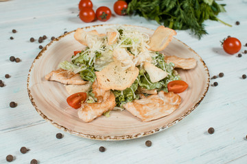 Fresh salad caesar closeup on brown plate on white textured table with cherry tomatoes and chilli and pepper spices and green at background