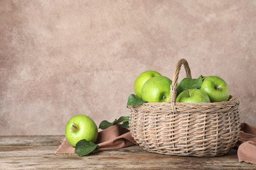 Composition with juicy green apples in wicker basket on table. Space for text