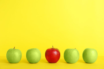 Row of green apples with red one on color background. Be different