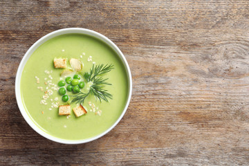 Fresh vegetable detox soup made of green peas in dish on wooden background, top view with space for text
