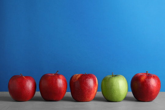 Row Of Red Apples With Green One On Table Against Color Background. Be Different