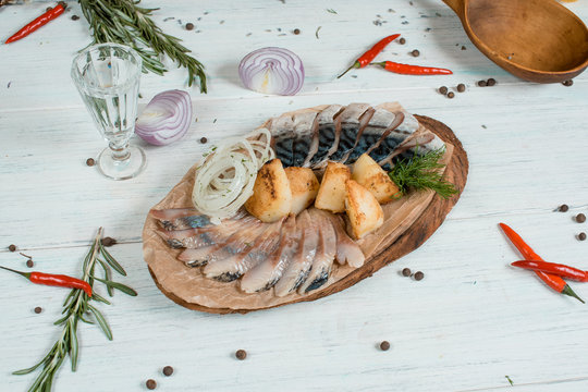 herring pieces and popato on wood desk on white table with onion and spices at background
