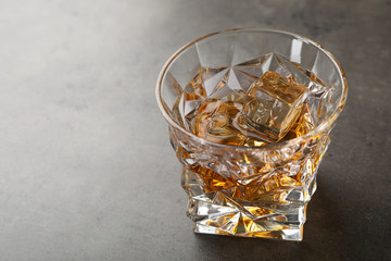 Golden whiskey in glass with ice cubes on table. Space for text