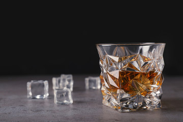 Golden whiskey in glass with ice cubes on table. Space for text