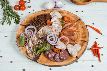 sliced ​​meat and sausage and basturma on a wood plate on white table with spices and chilli and green on background