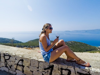 Frau trinkt Wein auf einer Mauer über der kroatischen Adria