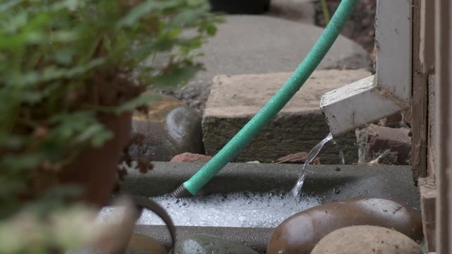 Closeup on a downspout on a house, water pouring onto a concrete splash block.