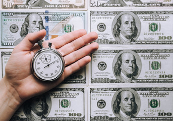 Time for quick money. Woman's hand holding a grey stopwatch over dollars background. Credit...