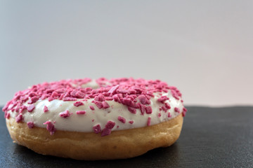 White glazed donut with pink sprinkles on black board and copy space