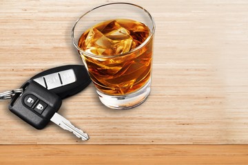Glass of whiskey and car key on wooden background