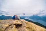 Rear view of couple looking map while sitting on mountain against cloudy sky