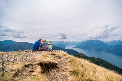 Rear view of couple looking map while sitting on mountain against cloudy sky