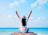 Rear view of woman with hands raised sitting on wooden pier by the sea