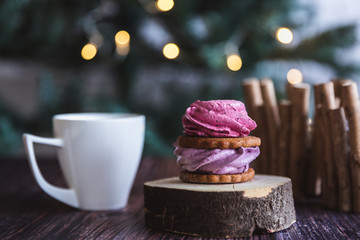 Obraz na płótnie Canvas Close up of homemade pink and purple zephyr or marshmallow in powdered sugar with white mug on wooden with abstract bokeh background. Black currant, blueberry marshmallows.