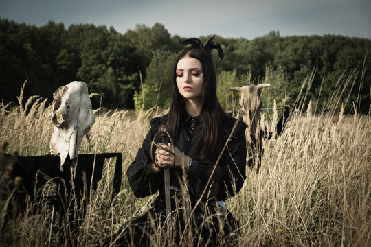 Gothic girl with a sword in her hands next to the skull of a cow on a pole