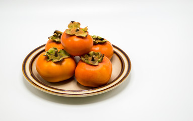 ripe orange persimmons stacked on a plate isolated on white