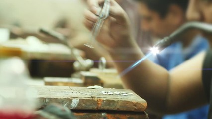 Artisans using tools to fabricate silver jewelry in a workshop. Crafstman welds silver jewelry piece 