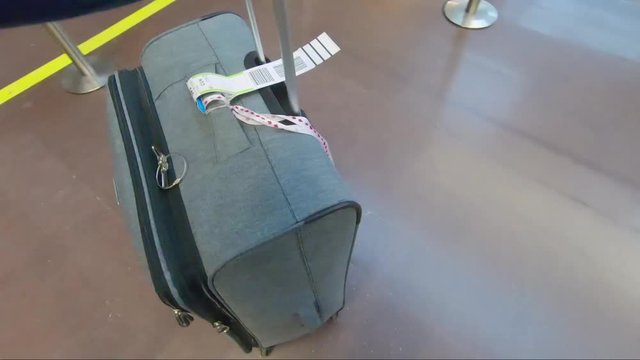 A passenger pushing the luggage on wheels at the airport baggage drop.
