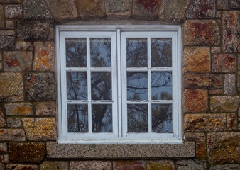 Fototapeta na wymiar Double-paned window in white reflects bare coniferous pine trees through the panes surounded with rugged warm-toned brick