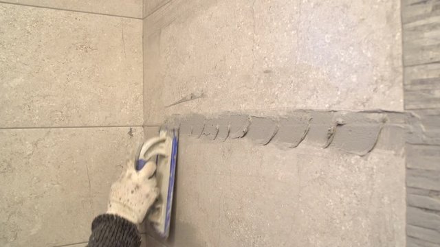 Worker putting fugue on the wall in bathroom. Grouting ceramic tiles, close up