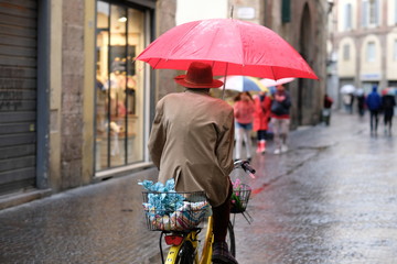 Italian man riding his bike through a cobble stoned village hold a red umbrella #1