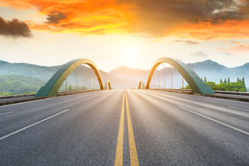 Asphalt road and mountains with bridge at beautiful sunset
