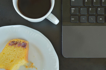 Cornmeal Cake with guava paste with a bite, beside a cup of coffee and part of a computer keyboard seen from top