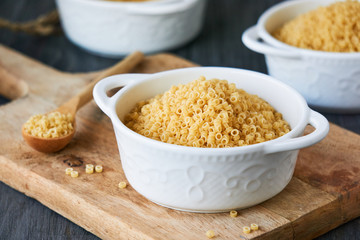 Uncooked anellini pasta in a bowl on wooden background