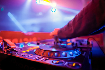 Obraz premium Club dj playing music on party.Nightclub disc jockey adjust sound frequency on professional sound mixer panel.Focus on djs hands holding regulator